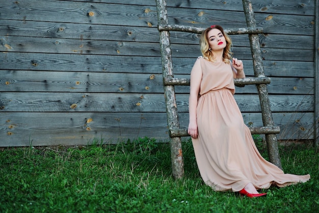 Chica rubia de elegancia Yong en vestido rosa en la escalera de madera de fondo del jardín