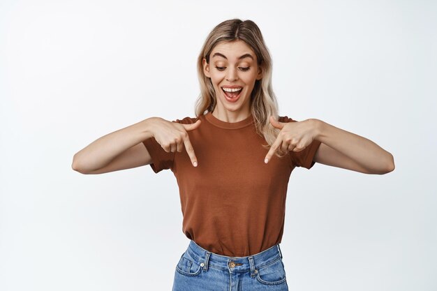 Chica rubia emocionada mirando y apuntando hacia abajo en el anuncio de venta del logotipo debajo que muestra un cartel con una sonrisa feliz de fondo blanco