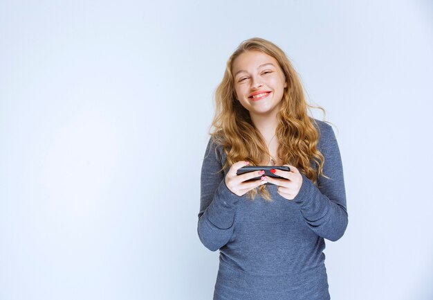 Chica rubia enviando mensajes de texto y mensajes con su teléfono inteligente.