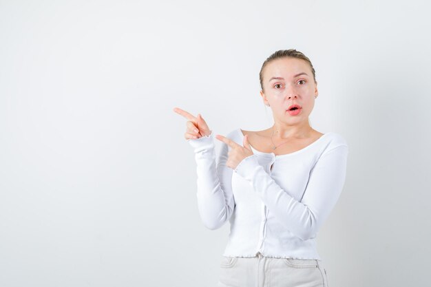 Chica rubia está apuntando su lado izquierdo sobre fondo blanco.