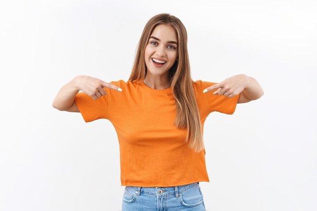 Chica rubia con estilo confiada, estudiante universitaria fanfarroneando, señalando con el dedo ella misma y sonriendo orgullosa