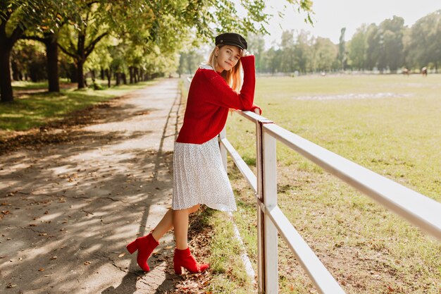 Chica rubia con estilo de pie en el camino del parque bajo los árboles amarillos.