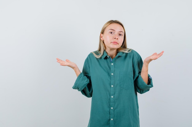 Chica rubia estirando las manos de manera interrogante en blusa verde y mirando desconcertado