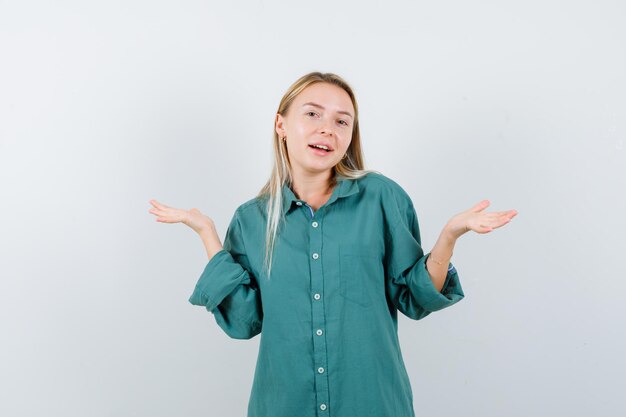 Chica rubia estirando las manos de manera interrogante en blusa verde y mirando perplejo