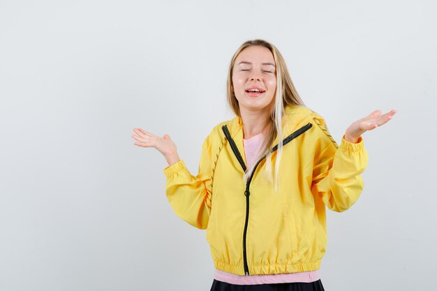 Chica rubia estirando las manos de manera interrogante en camiseta rosa y chaqueta amarilla y mirando perplejo.