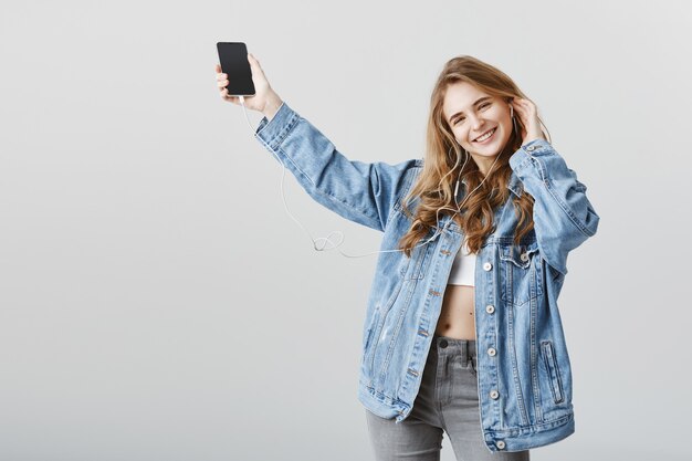 Chica rubia feliz despreocupada bailando con música en auriculares, sonriendo alegre