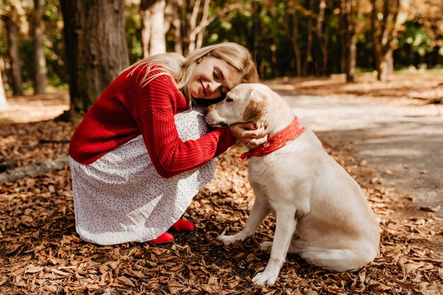 Chica rubia felizmente feliz sonriendo cerca de su perro. Hermosa mujer feliz con amada mascota.