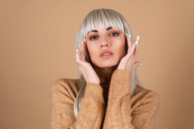 Chica rubia con flequillo y maquillaje diurno marrón en un suéter sobre fondo beige retrato de moda sensual