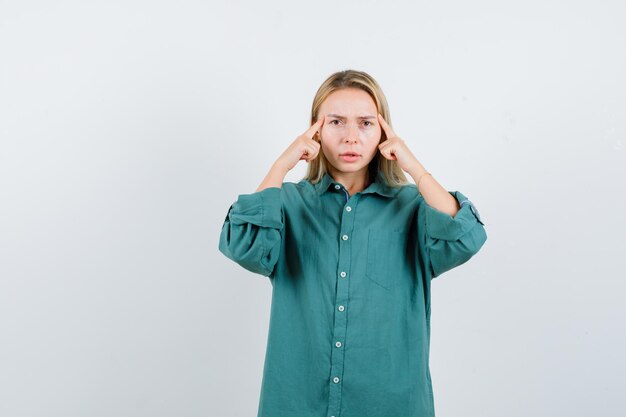 Chica rubia frotando las sienes en blusa verde y mirando seria