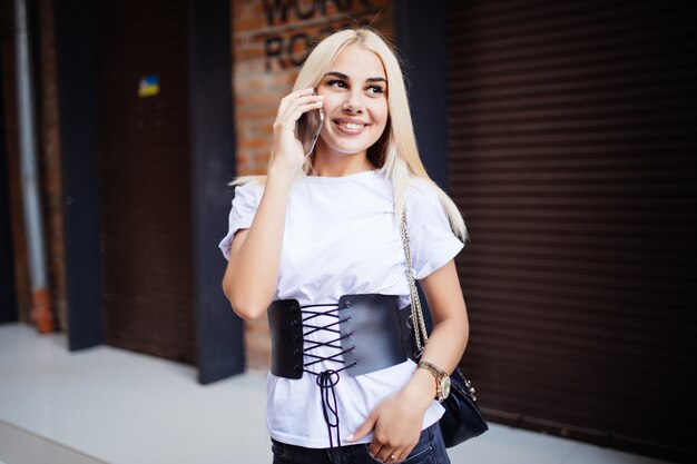 Chica rubia hablando por teléfono móvil en la pared de piedra
