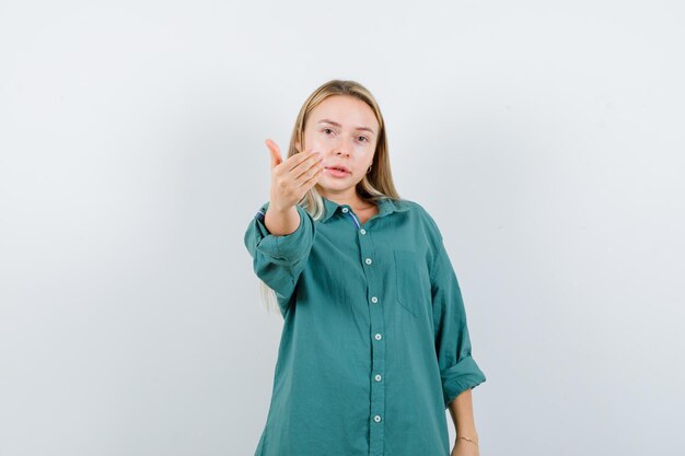 Chica rubia invitando a venir en blusa verde y luciendo amable