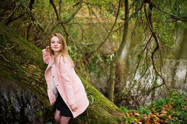 Chica rubia joven en abrigo rosa posó en el parque de otoño
