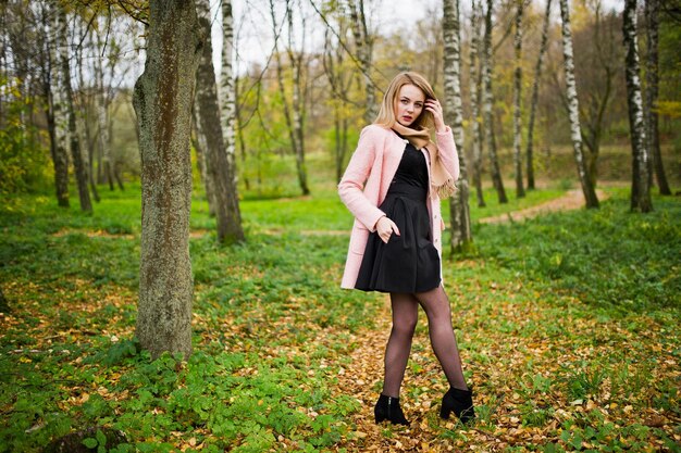Chica rubia joven en abrigo rosa posó en el parque de otoño