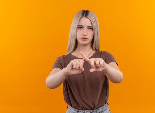 Chica rubia joven de aspecto serio gesticulando no en el espacio naranja aislado con espacio de copia