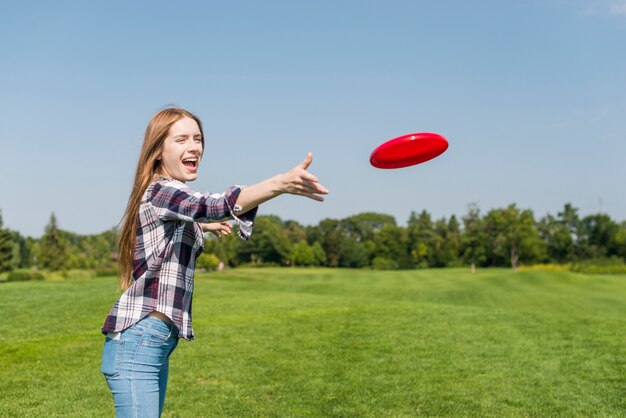 Chica rubia lanzando un frisbee rojo