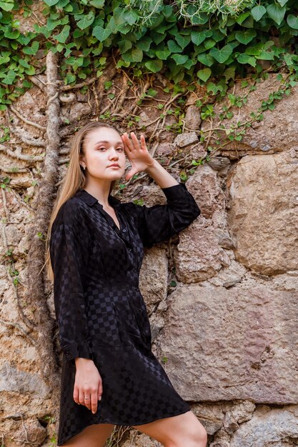 La chica rubia mira a la izquierda con vestido negro sobre fondo de piedra