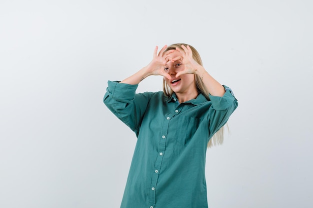 Chica rubia mostrando gesto de amor con las manos en blusa verde y luciendo bonita