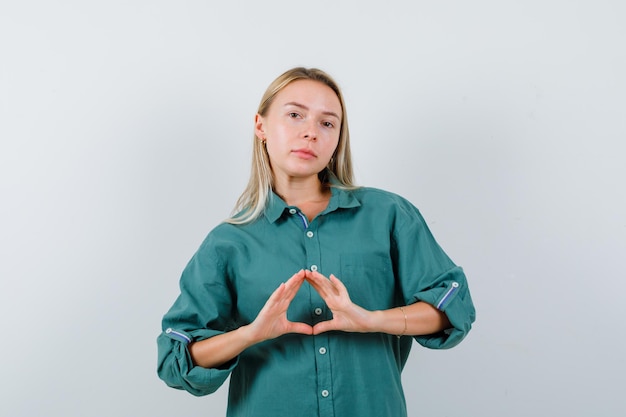 Chica rubia mostrando gesto de seguro en blusa verde y luciendo radiante