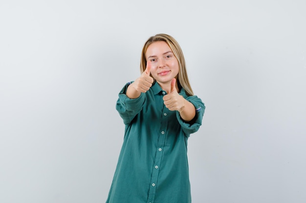 Foto gratuita chica rubia mostrando los pulgares para arriba con ambas manos en blusa verde y mirando impresionado