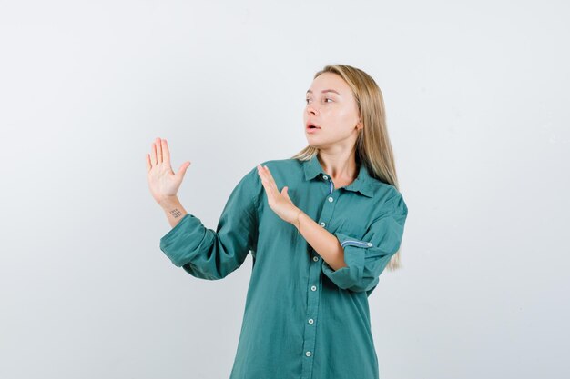 Chica rubia mostrando señales de alto en blusa verde y mirando seria.