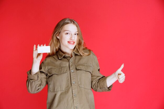 Chica rubia mostrando su tarjeta de visita y signo de mano positivo.