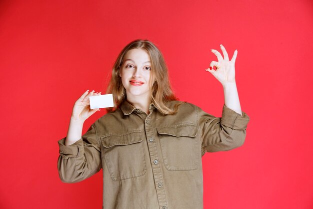 Chica rubia mostrando su tarjeta de visita y signo de mano positivo.
