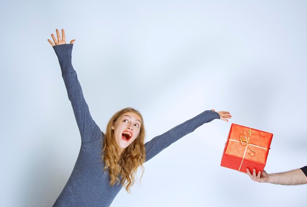 A una chica rubia se le ofrece una caja de regalo roja y está ansiosa por llevársela.