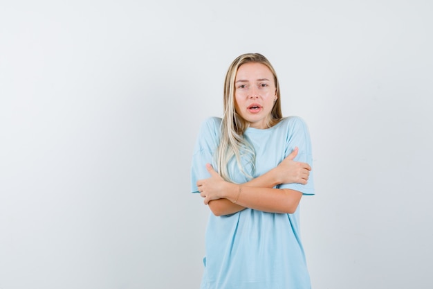 Foto gratuita chica rubia de pie con los brazos cruzados en camiseta azul y mirando serio, vista frontal.