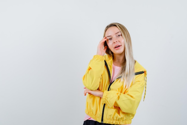 Chica rubia de pie en pose de pensamiento en chaqueta amarilla y bonita