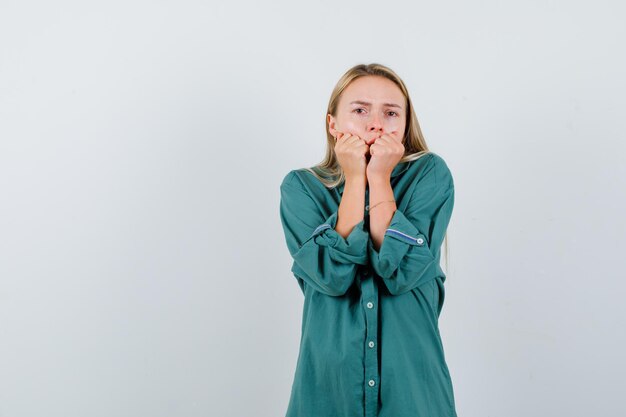 Chica rubia poniendo las manos en la boca en blusa verde y mirando sorprendido