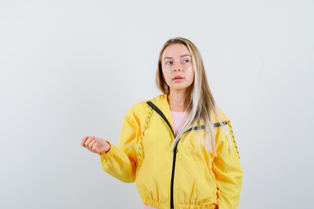 Chica rubia posando mientras mira a un lado en chaqueta amarilla y parece curioso