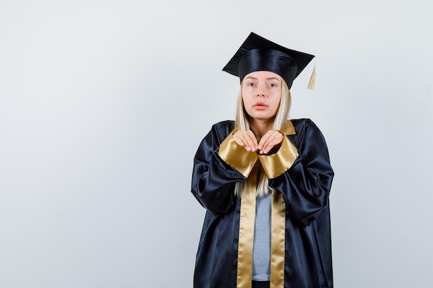 Foto gratuita chica rubia que invita a venir con toga y birrete de graduación y se ve afable.