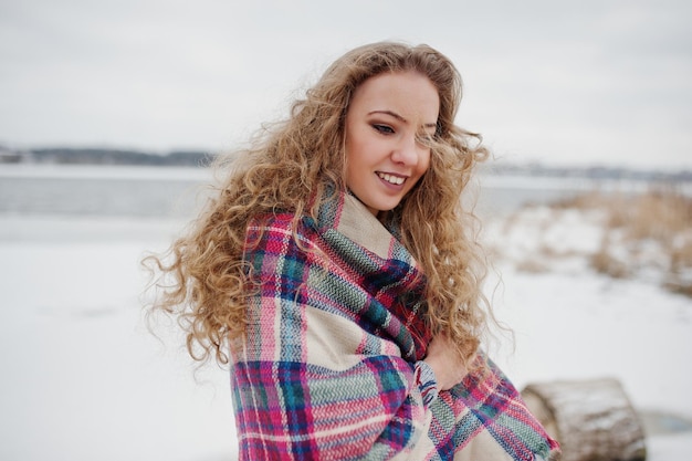 Chica rubia rizada en cuadros a cuadros contra el lago congelado en el día de invierno