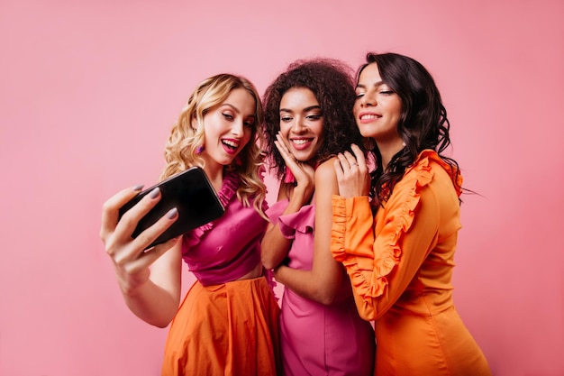 Chica rubia romántica haciendo selfie con amigos Bellas damas posando sobre fondo rosa