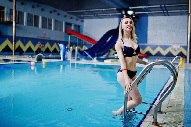 Chica rubia sexy en traje de baño azul descansando en la piscina del parque acuático