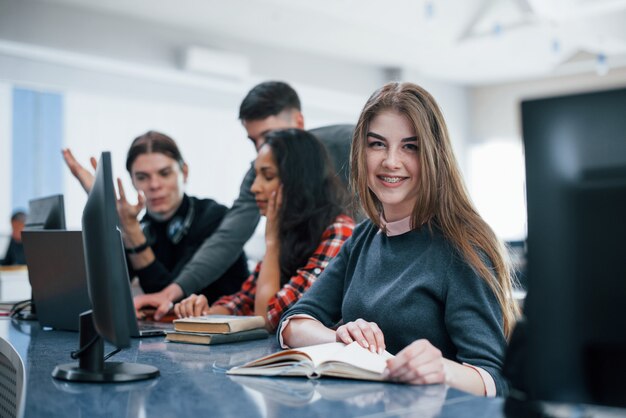 Chica rubia sonriendo. Grupo de jóvenes en ropa casual que trabajan en la oficina moderna