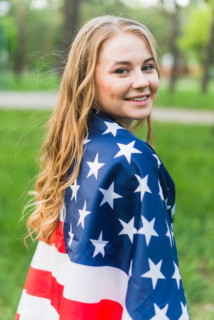 Chica rubia sonriente con bandera americana en la naturaleza