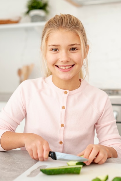 Chica rubia sonriente cortando pepino