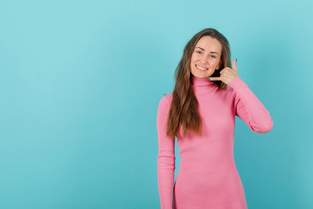 Chica rubia sonriente está mostrando un gesto móvil sosteniendo la mano cerca de la oreja sobre fondo azul.