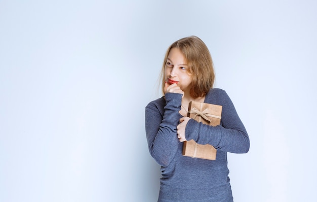 Chica rubia sosteniendo una caja de regalo de cartón y parece confundida y pensativa.