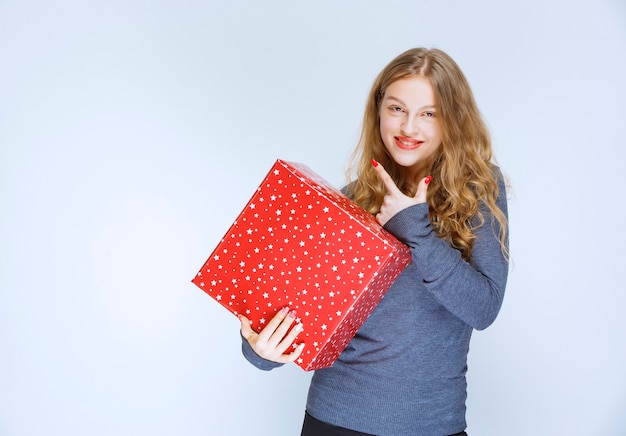 Chica rubia sosteniendo una caja de regalo roja grande.