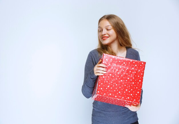 Chica rubia sosteniendo una caja de regalo roja grande.