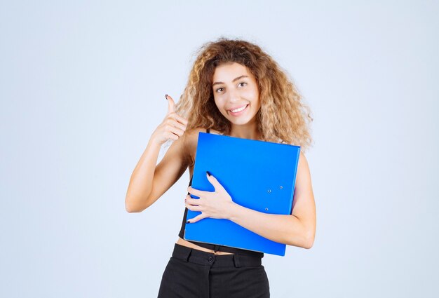 Chica rubia sosteniendo una carpeta azul con confianza.