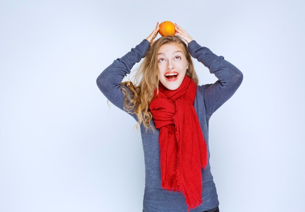 Chica rubia sosteniendo frutas naranjas sobre su cabeza.