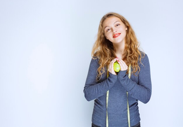 Chica rubia sosteniendo una manzana verde en sus palmas.