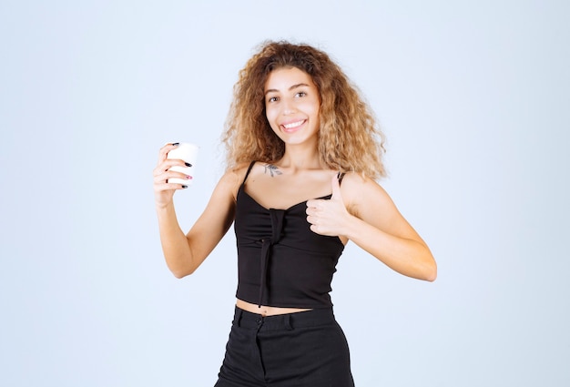 Chica rubia sosteniendo una taza de café y mostrando que le gustaba el sabor.