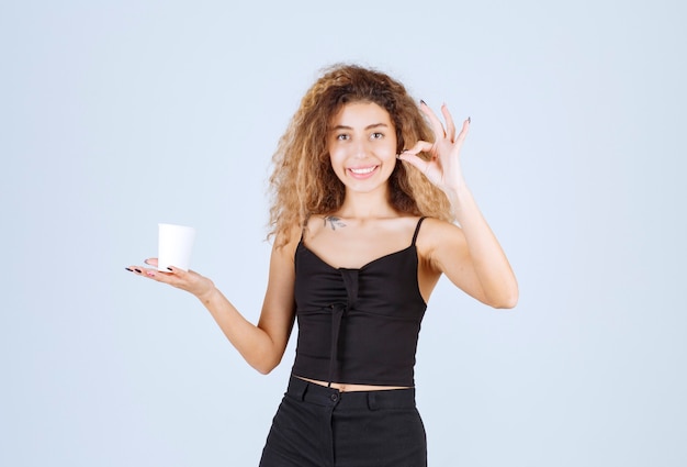 Chica rubia sosteniendo una taza de café y mostrando que le gustaba el sabor.
