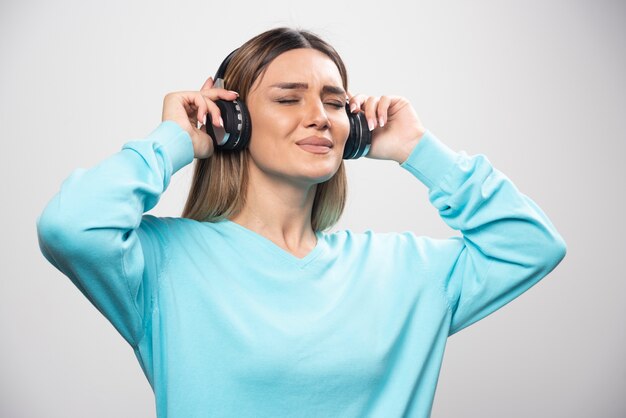 Chica rubia en sudadera azul con auriculares, disfrutando de la música y divirtiéndose