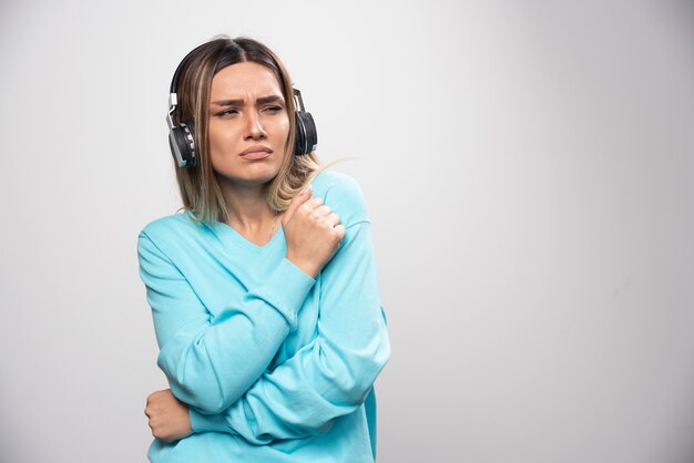 Chica rubia en sudadera azul con auriculares y tratando de entender la música.