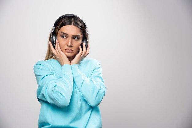 Chica rubia en sudadera azul con auriculares y tratando de entender la música.